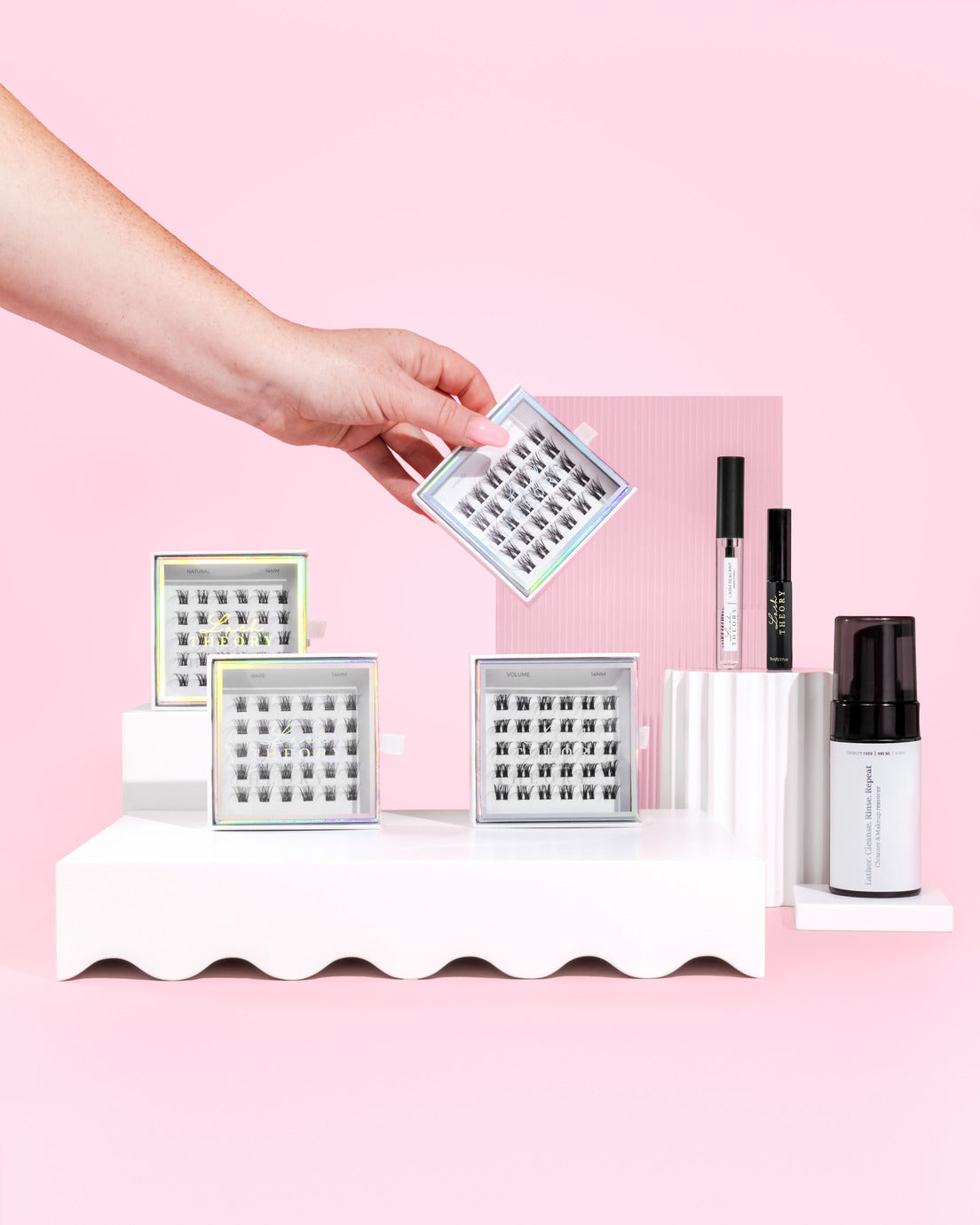 A hand going into a pick up a box of eye lashes. There are other products from the lash system.